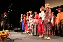 Grupa osób w tradycyjnych strojach ludowych podczas występu na scenie.