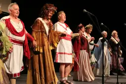 Grupa osób w strojach historycznych, występujących na scenie.