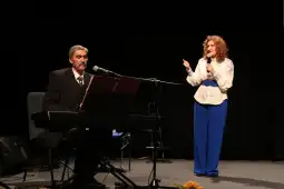 Mężczyzna gra na pianinie, a kobieta śpiewa na scenie.