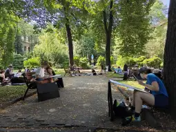 Grupa osób rysujących w parku, otoczona zielenią i drzewami.