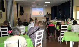Spotkanie seniorów z prelekcją Wojciecha Botwina w sali z zielonymi obrusami.