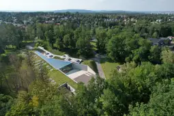 Nowoczesny budynek w otoczeniu zieleni, z dużymi przeszklonymi powierzchniami.