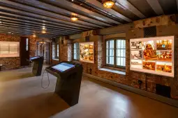 Wnętrze muzeum z interaktywnymi stanowiskami i wystawionymi zdjęciami na ścianach.