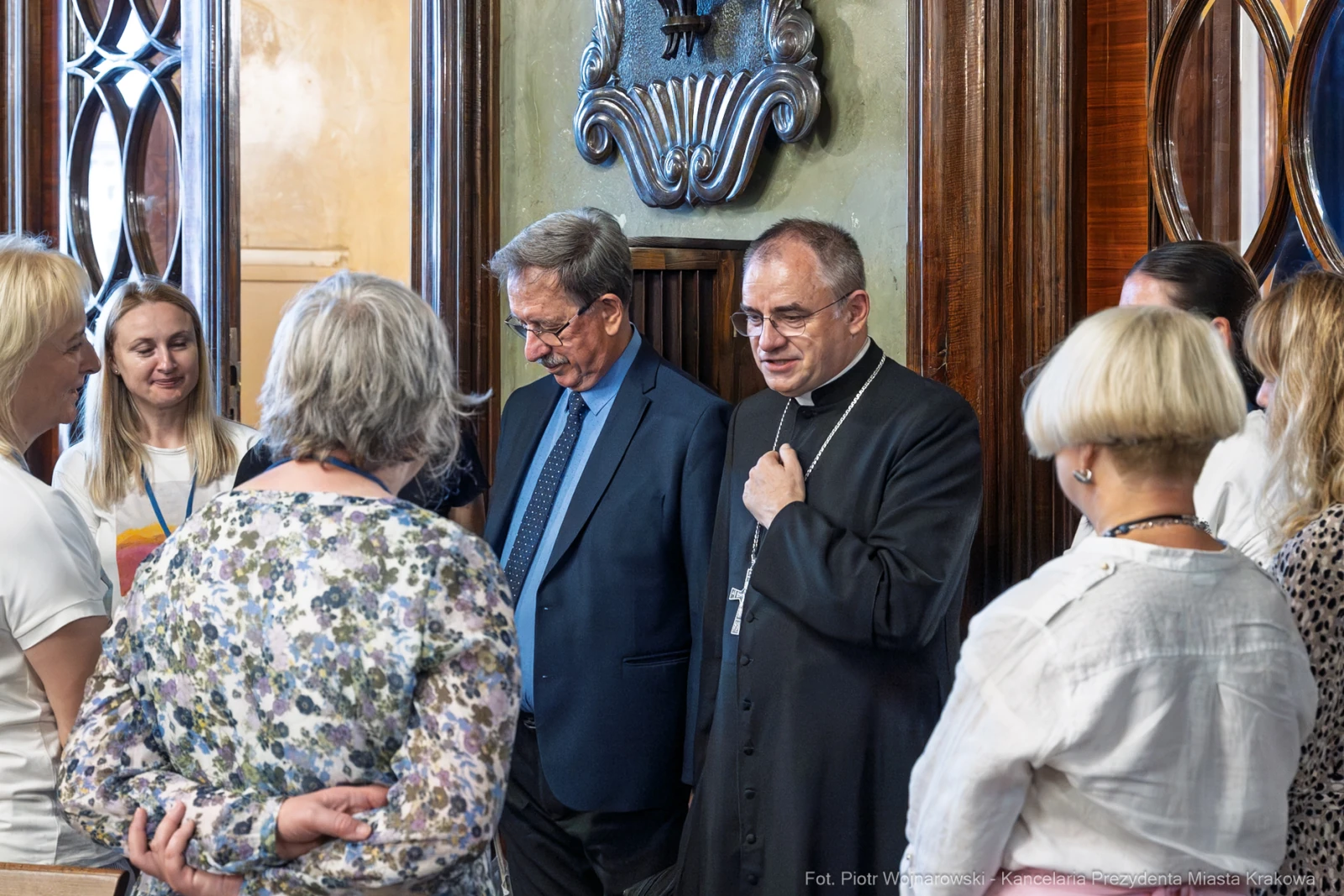 Grupa osób rozmawia w eleganckim wnętrzu, wśród nich duchowny i mężczyzna w garniturze.  Autor: Piotr Wojnarowski