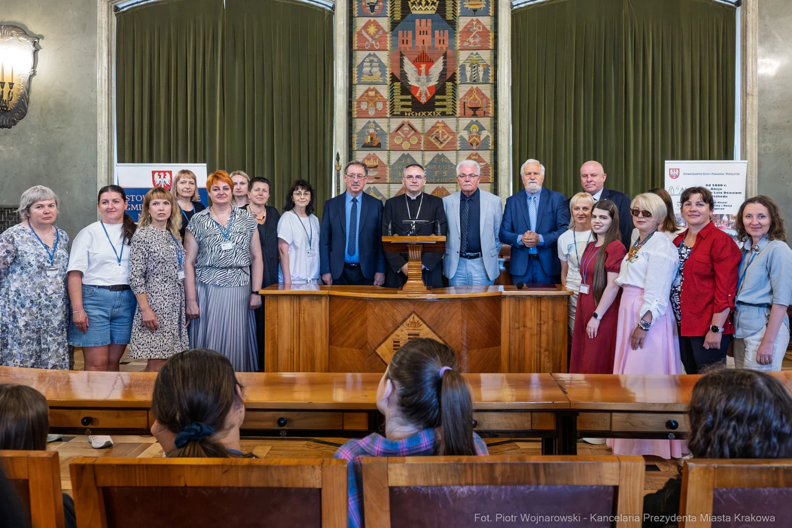 Grupa ludzi w sali, w tle herb miasta, podczas uroczystości lub spotkania.  Autor: Piotr Wojnarowski