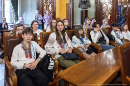 Grupa dzieci w tradycyjnych strojach, siedzących w sali obrad.