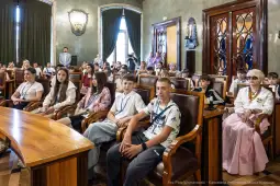 Grupa dzieci i młodzieży siedząca w sali obrad, w tle eleganckie wnętrze.