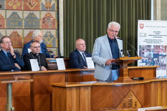 Mężczyzna przemawia w sali obrad, w tle siedzą inni uczestnicy wydarzenia.