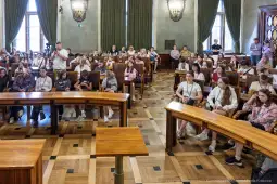 Grupa ludzi siedząca w sali, uczestnicząca w wydarzeniu lub spotkaniu.