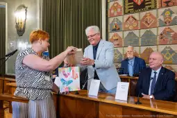 Wręczenie nagrody w sali obrad z uśmiechniętymi uczestnikami.