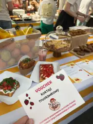 Stół z jedzeniem, w tym koktajl truskawkowy, owoce i wypieki. Widoczny voucher na koktajl.