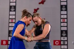 Dwie kobiety rywalizują w wspinaczce sportowej, z intensywnym skupieniem na twarzach.