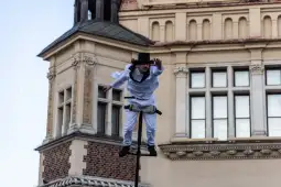 Mężczyzna w białym stroju balansujący na linie nad budynkiem.