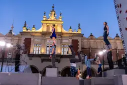 Grupa akrobatów wykonujących skomplikowane figury na tle oświetlonego budynku.