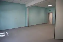 Pusty pokój z niebieskimi ścianami i jasną podłogą, z drzwiami prowadzącymi do innego pomieszczenia.