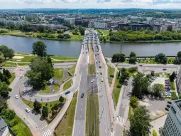Widok na most nad rzeką z otaczającą infrastrukturą miejską i zielenią.