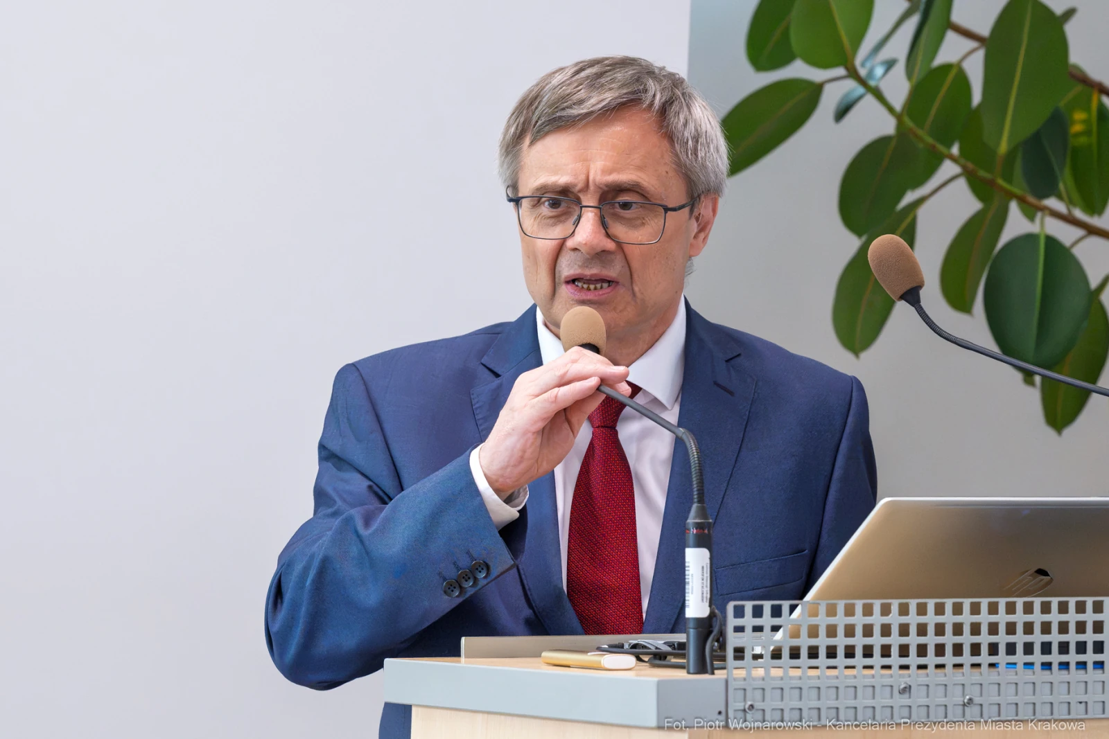 Mężczyzna w garniturze przemawia do mikrofonu, stojąc przy biurku z laptopem.  Autor: Piotr Wojnarowski