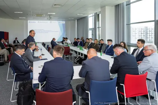 Spotkanie biznesowe z uczestnikami przy długim stole w nowoczesnej sali konferencyjnej.