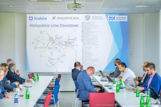 Spotkanie dotyczące Małopolskich Linii Dowozowych z mapą i uczestnikami przy stole.