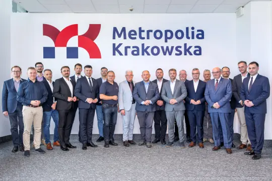 Grupa mężczyzn w garniturach stojąca przed napisem Metropolia Krakowska.