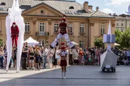 Grupa artystów ulicznych wykonujących akrobacje i sztuczki w tłumie ludzi.