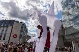 Wielkie białe figury na szczudłach podczas wydarzenia ulicznego, tłum ludzi w zachwycie.