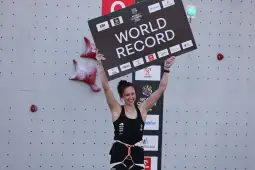 Kobieta trzymająca tablicę z napisem WORLD RECORD na tle ścianki wspinaczkowej.