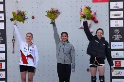 Trzy zawodniczki wspinaczki sportowej na podium z bukietami kwiatów.