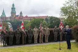 Ceremonia wojskowa z żołnierzami w mundurach i mówcą na tle zamku.