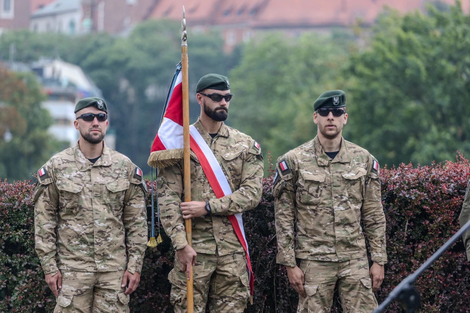 Trzej żołnierze w mundurach wojskowych, jeden z flagą, stoją w postawie defiladowej.  Autor: Bogusław Świerzowski