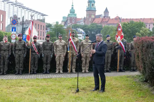 Ceremonia wojskowa z mężczyzną przemawiającym do zgromadzonego tłumu żołnierzy.
