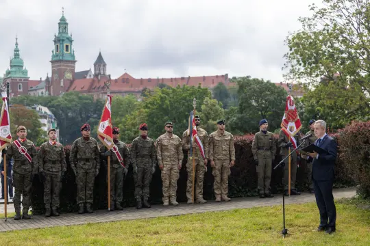 Ceremonia wojskowa z żołnierzami w mundurach i mówcą na tle zamku.