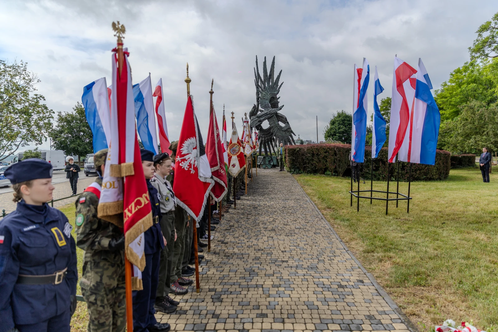 Uroczystość z flagami narodowymi i pomnikiem w tle.  Autor: Bogusław Świerzowski