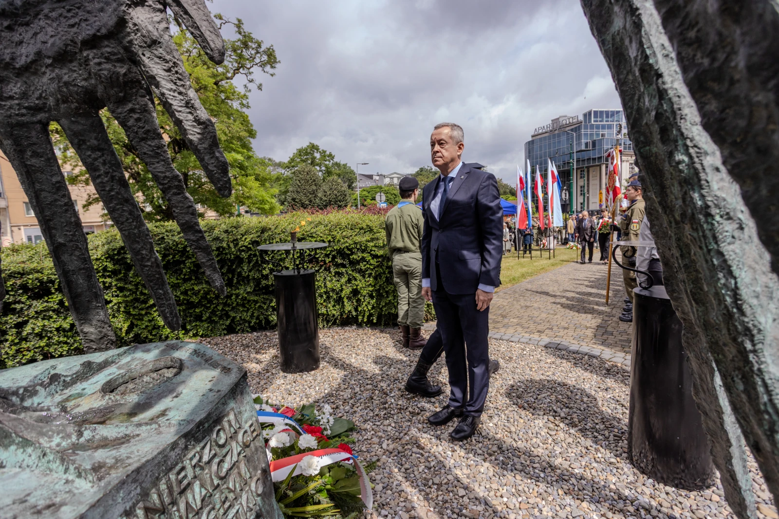 Mężczyzna w garniturze stoi obok pomnika, w tle flagi i zieleń.  Autor: Bogusław Świerzowski