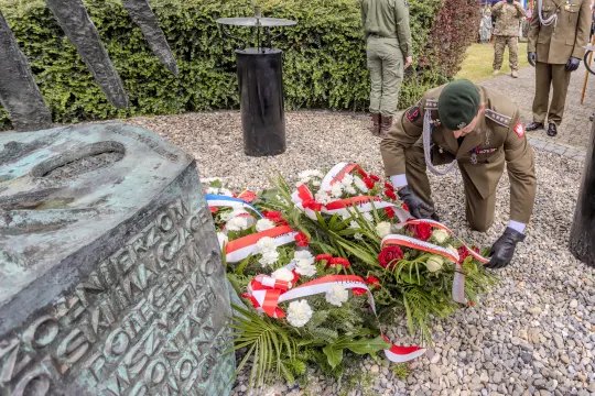 Żołnierz składa wieniec z kwiatów przy pomniku.