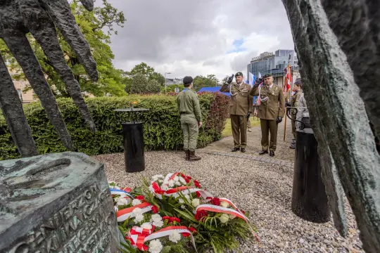 Ceremonia złożenia wieńców przy pomniku wojskowym z obecnością żołnierzy i flag.