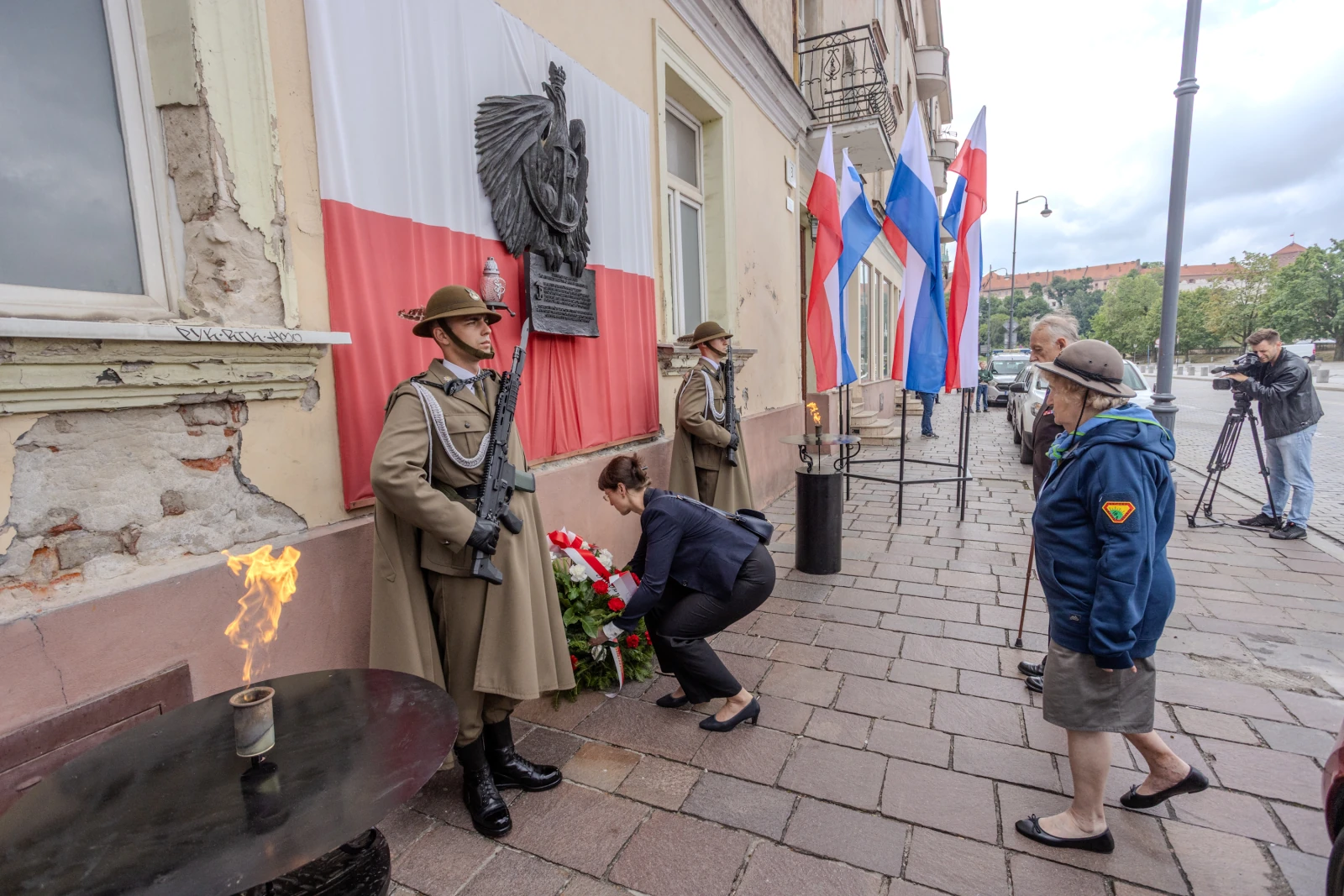 Uroczystość złożenia kwiatów przed budynkiem z flagami i wartą honorową.  Autor: Bogusław Świerzowski