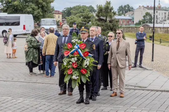 Uroczystość składania wieńca przez grupę ludzi w formalnych strojach.