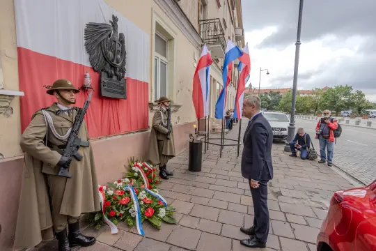 Uroczystość złożenia kwiatów przy pomniku, żołnierze w mundurach, flagi Polski i Rosji.