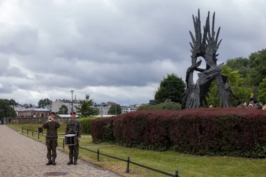 Dwaj żołnierze grają na trąbce i bębnie przed monumentalnym pomnikiem.