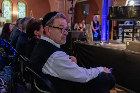 Mężczyzna w okularach i kapeluszu siedzi na widowni podczas wydarzenia kulturalnego.
