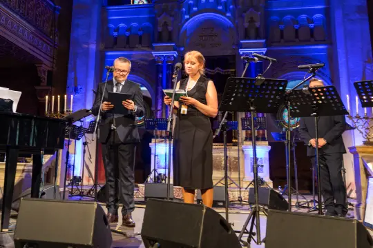 Dwójka mówców na scenie w kościele, obok instrumenty muzyczne i mikrofony.