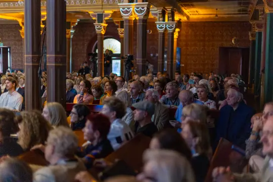 Tłum ludzi na wydarzeniu kulturalnym, skupionych na wystąpieniu.