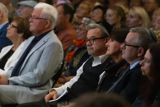 Grupa ludzi siedzących na widowni podczas wydarzenia, skupionych na wystąpieniu.