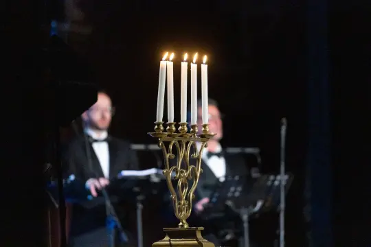 Świecznik z sześcioma płonącymi świecami w tle dwaj mężczyźni w garniturach.