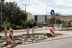 Zniszczona nawierzchnia torowiska tramwajowego z oznaczeniami drogowymi.