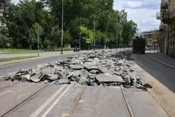 Zniszczona nawierzchnia drogi z gruzem i roślinnością w tle.
