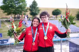 Młodzi sportowcy z medalami i kwiatami, ubrani w czerwone stroje reprezentacyjne.