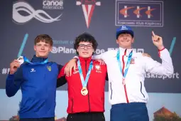 Trzech medalistów na podium zawodów kajakarskich, uśmiechnięci, z medalami na szyjach.