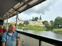 Mężczyzna siedzący na łodzi, widok na zamek i rzekę w tle.